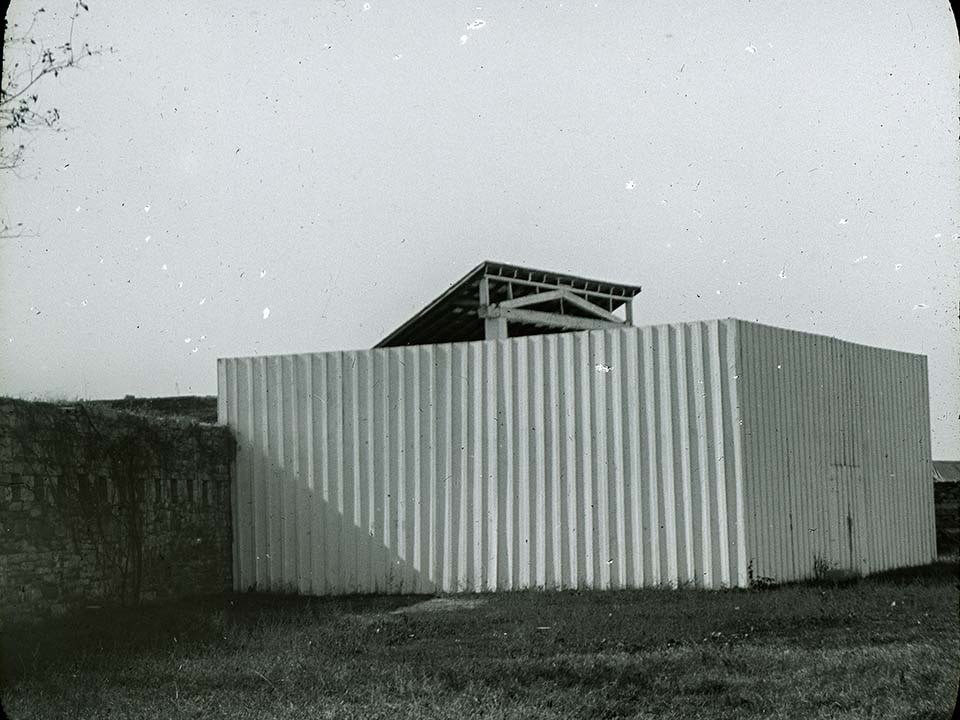 Tall white fence surrounds gallows only tip of slanted roof visible.