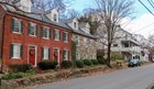 Color photo of several brick, stone, and wooden historic houses lining a street with cars