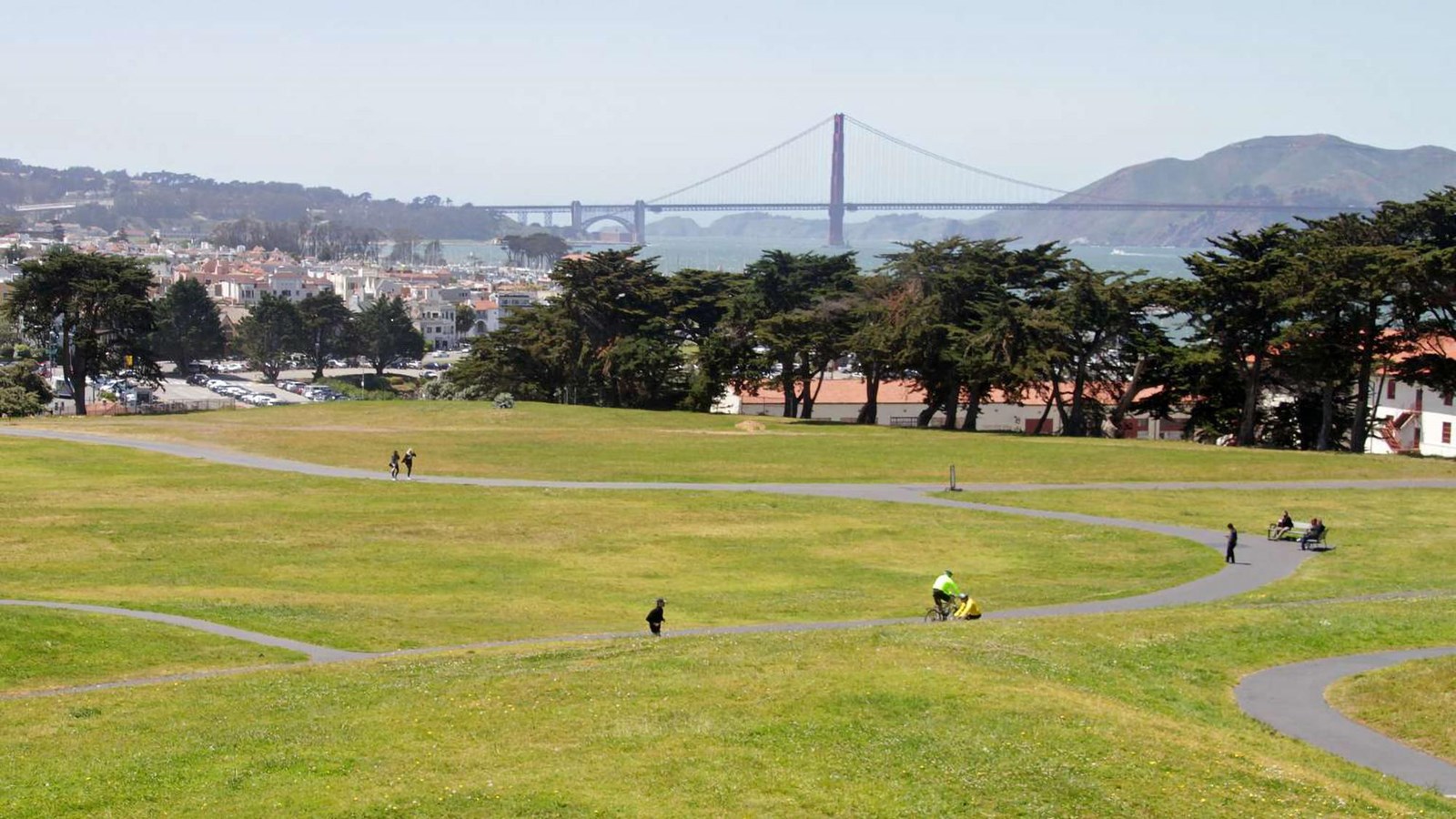 A view across the Great Meadow with winding paths through green grass and the Golden Gate Bridge. 