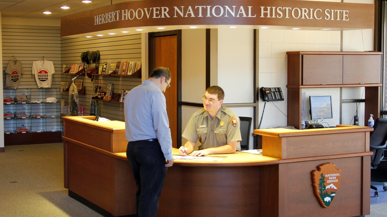 A uniformed ranger at an information desk assists a park visitor.