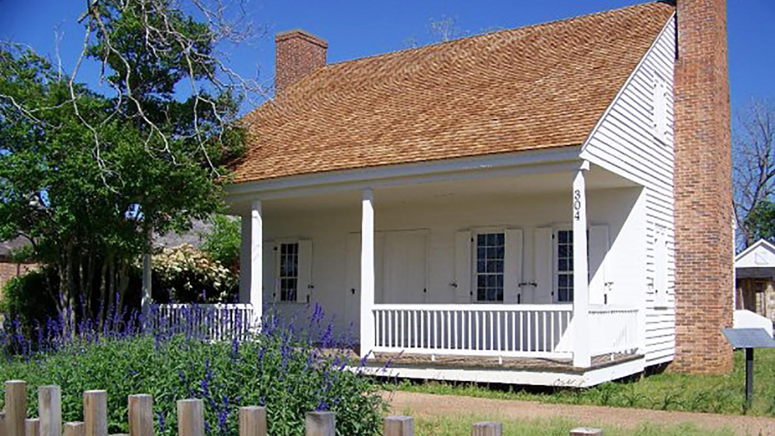 A small, white, cottage-like house with a shingled roof and double chimneys.