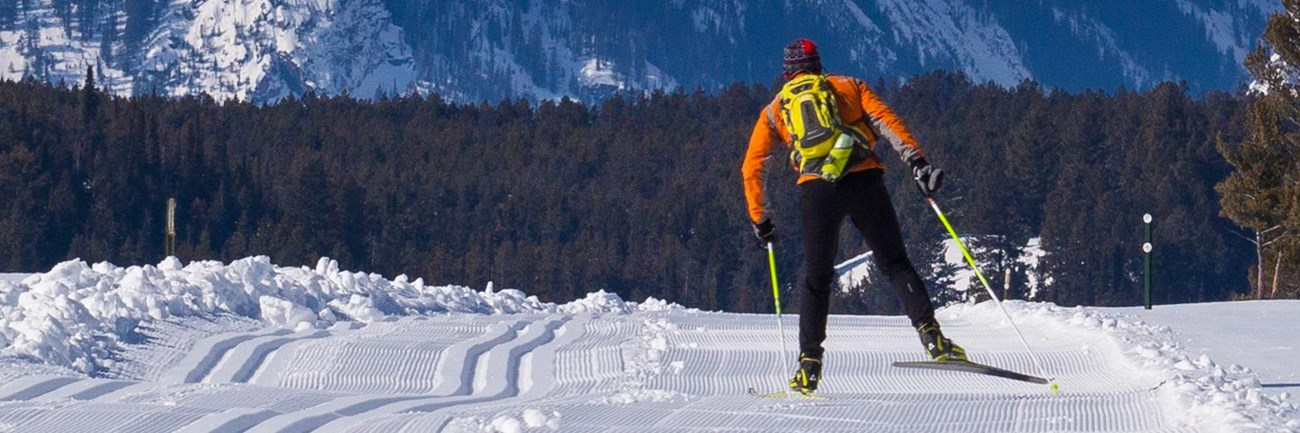 Skate skier on groomed Teton Park Road. Mountains rise in the distance.