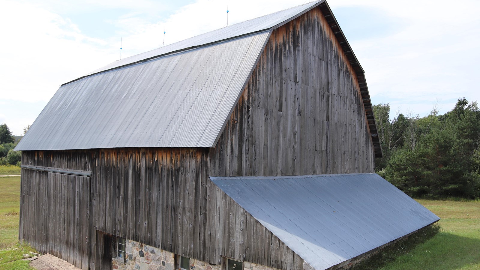 Grey faded wood and silver shining metal roof, the base along the hill made of cemented field stones