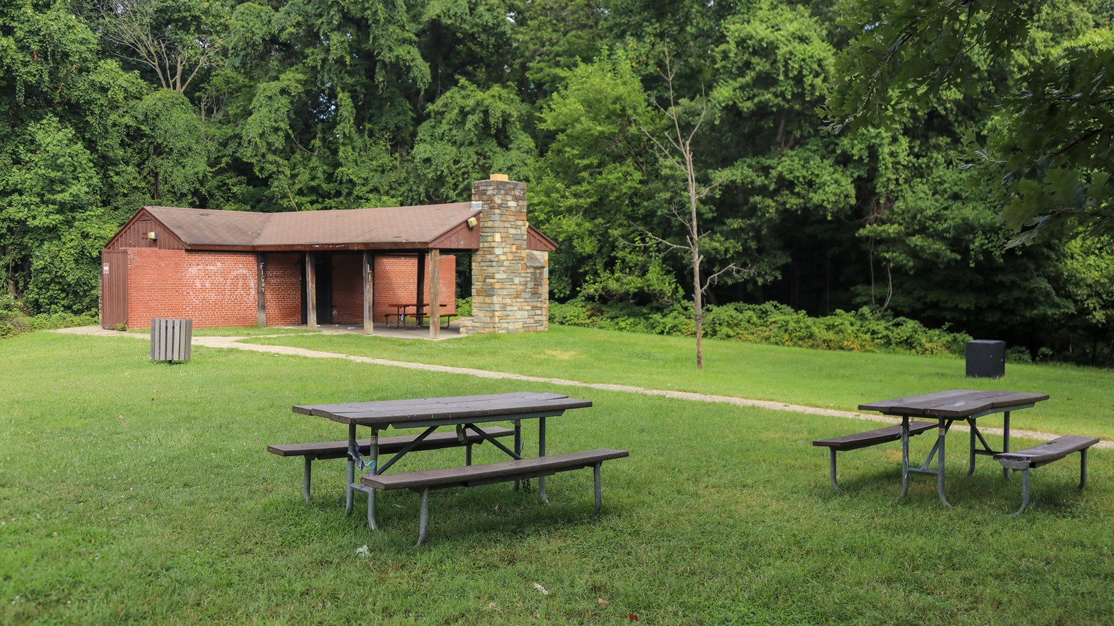 Two picnic tables in front of a large red building. 