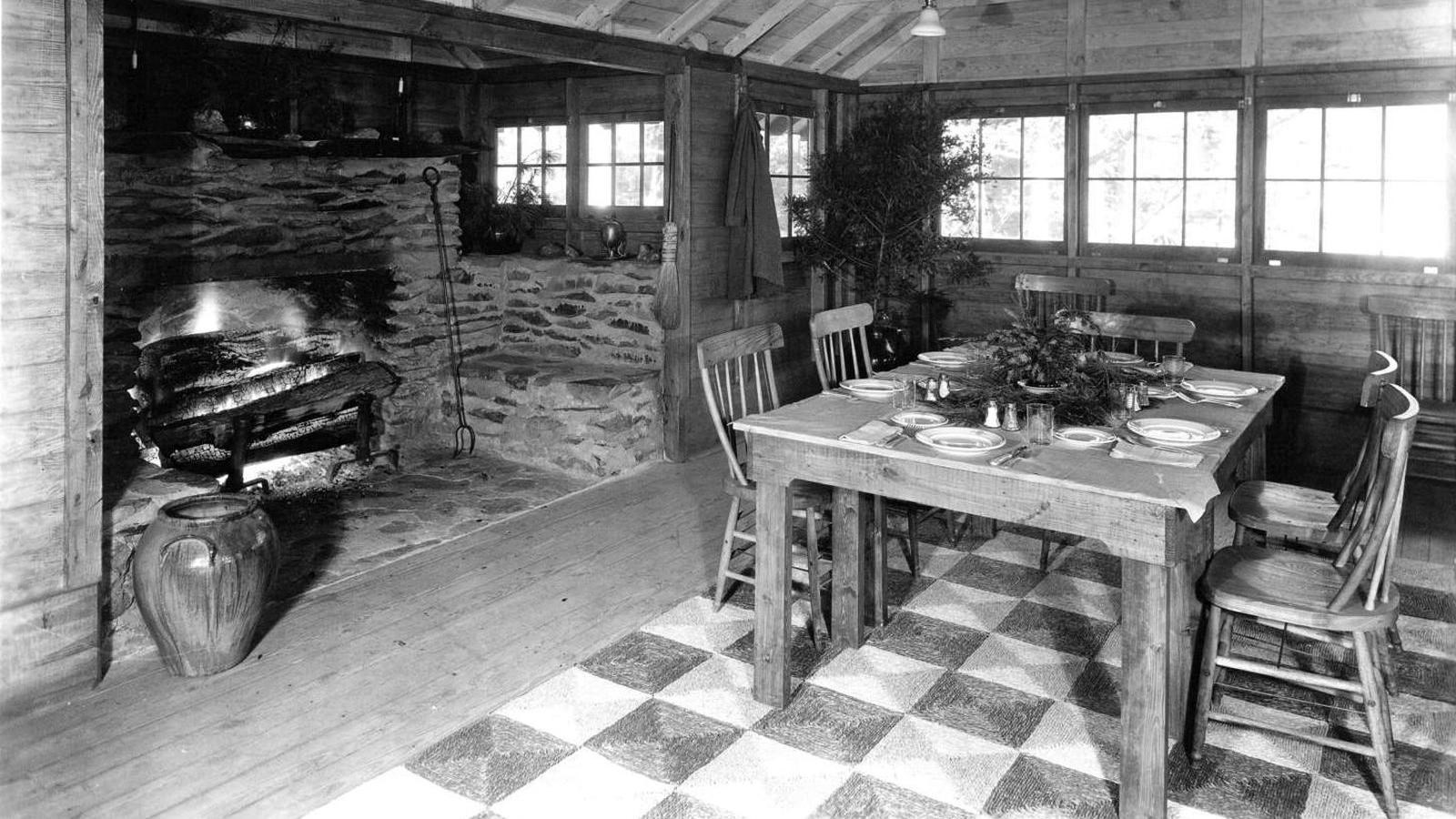 A black and white photo of wooden walls and vaulted ceiling above a set table with checkered floor.