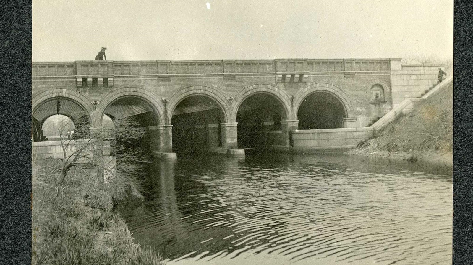Black and white of five arches in bridge with person on top. 
