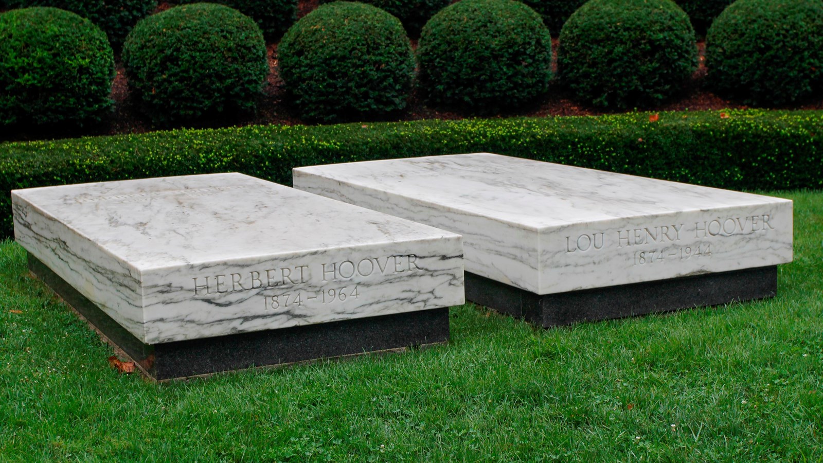 Two marble ledger stones each mark a grave in a semicircular landscaped plot with a flagpole.