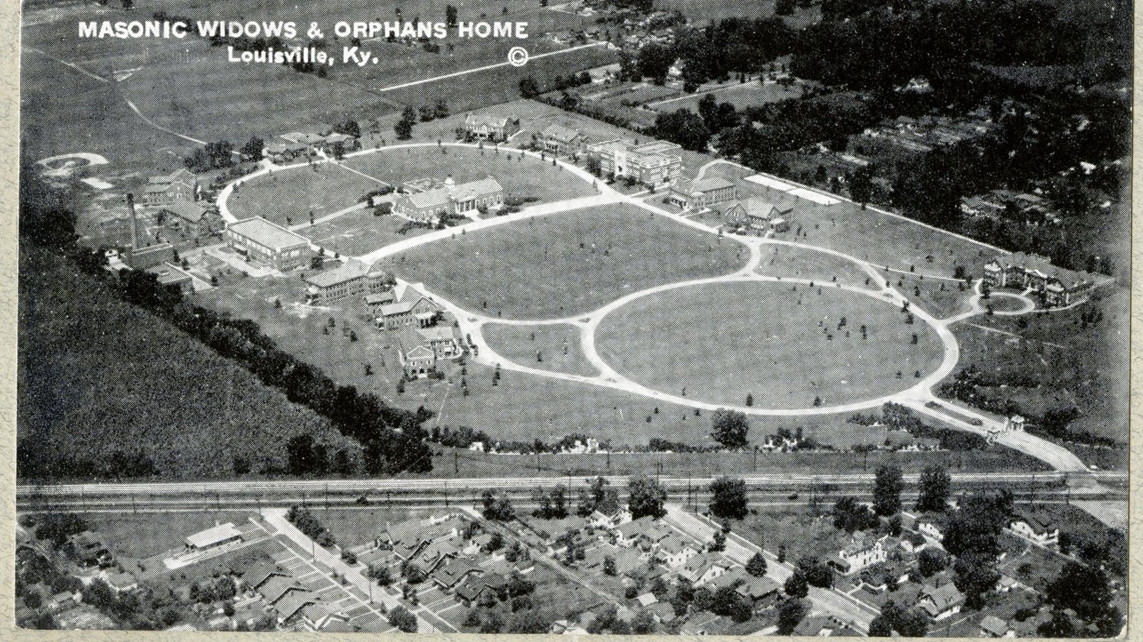 Black and white aerial of campus with curving paths, buildings on paths, open space in middle 