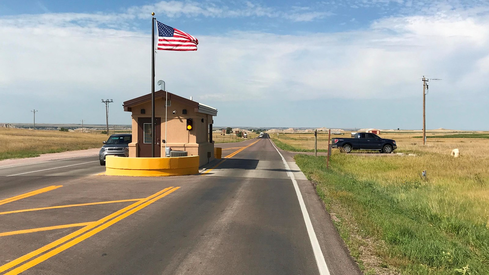 Single tan building in the middle of a paved road with USA flag under a blue sky.