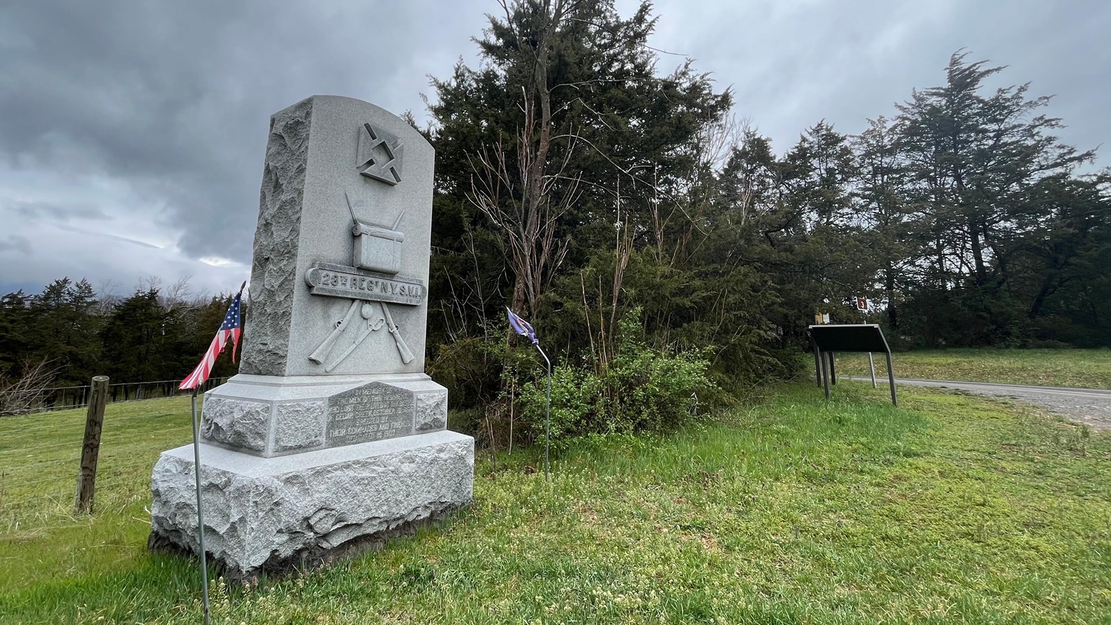 Large granite monument inscribed with 128th Reg NYSVI next to a row of trees. 