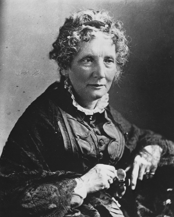 Black and white studio portrait of middle aged woman wearing high-necked dress and shawl