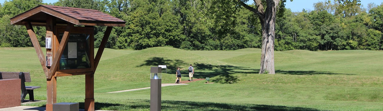 Two people walking into a grass-covered mound area