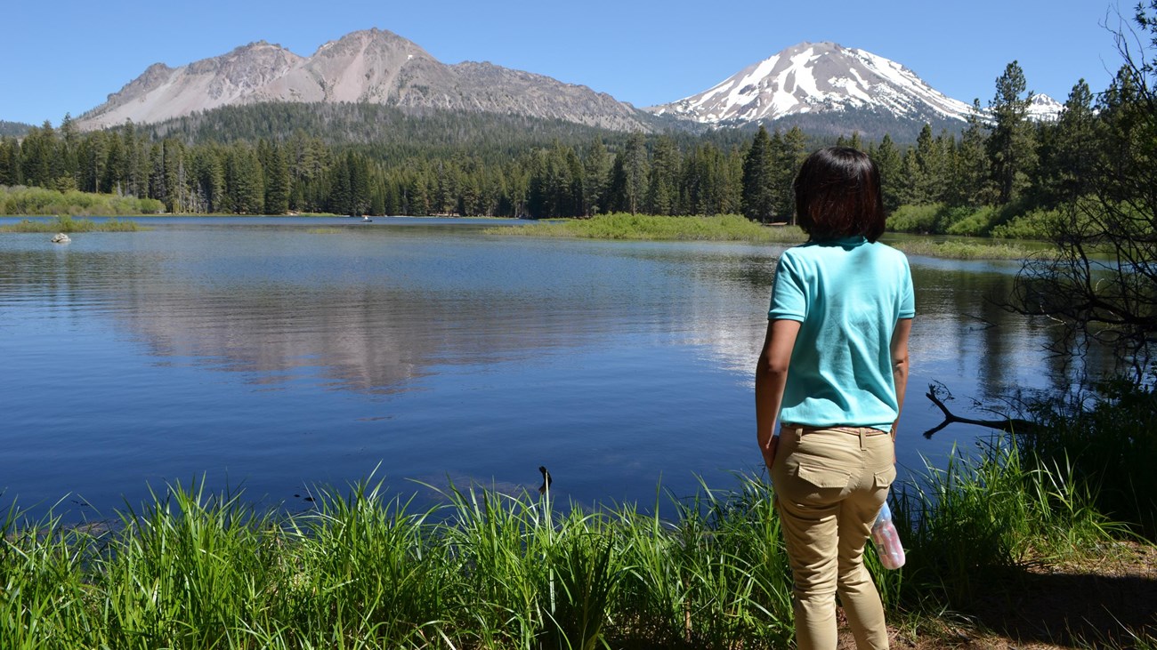 A looks out on a brush-lined lake backed by volcanic peaks.