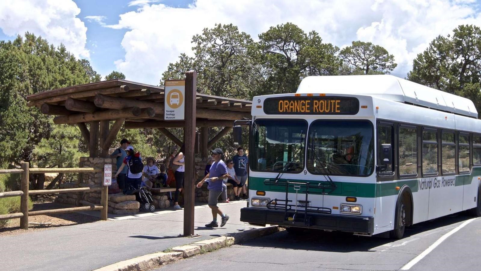 White and green shuttle bus is stopped at a sign, waiting for visitors to board.