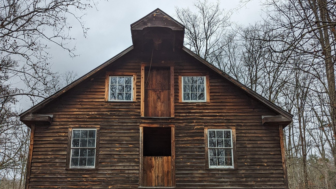 A wooden grist mill three stories tall surrounded by fallen leaves.