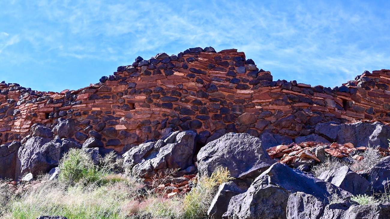 A red sandstone and black basalt pueblo sits atop a hill.