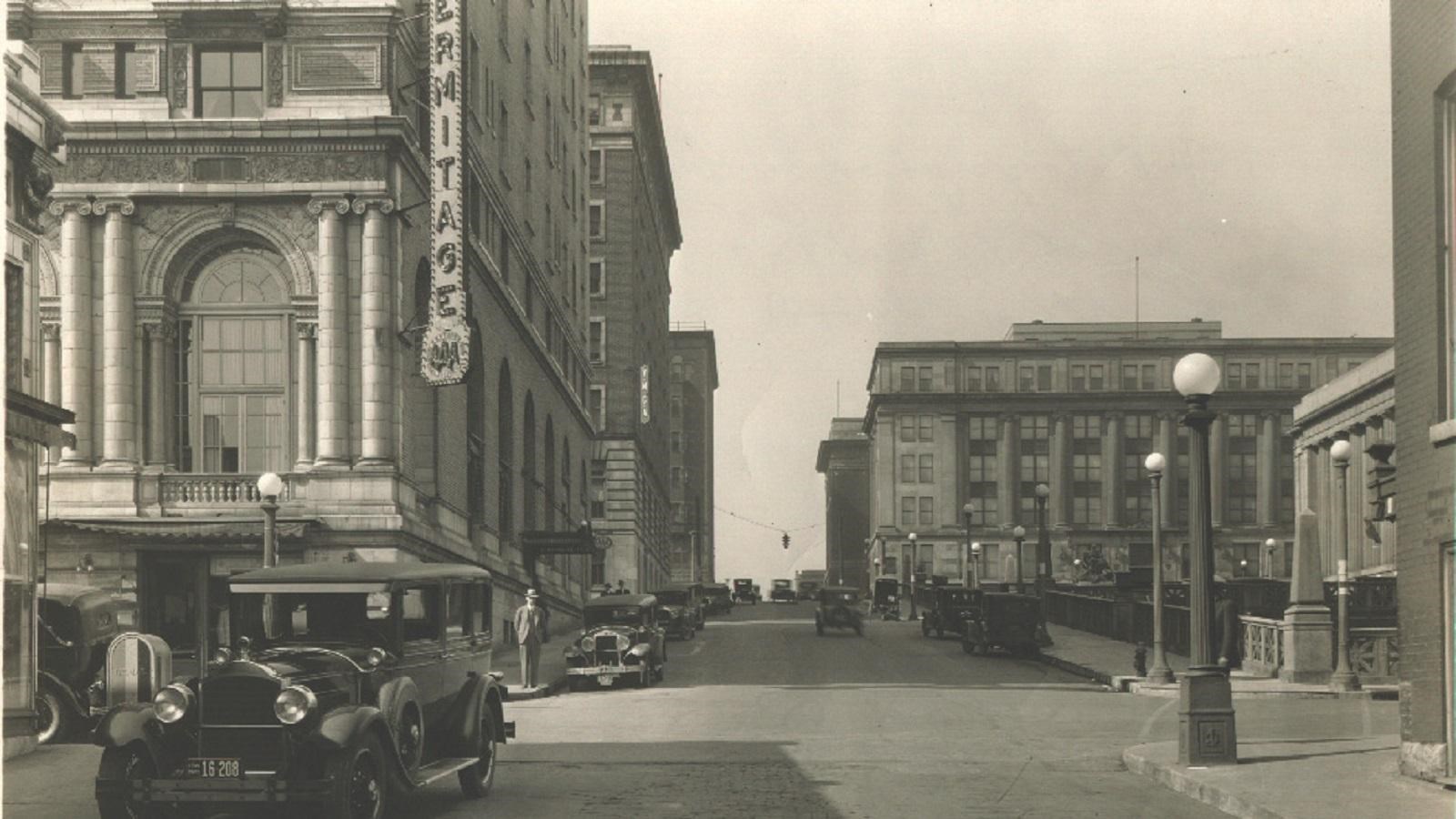 Black and white photo of city street, buildings including the Hermitage Hotel, and automobiles.