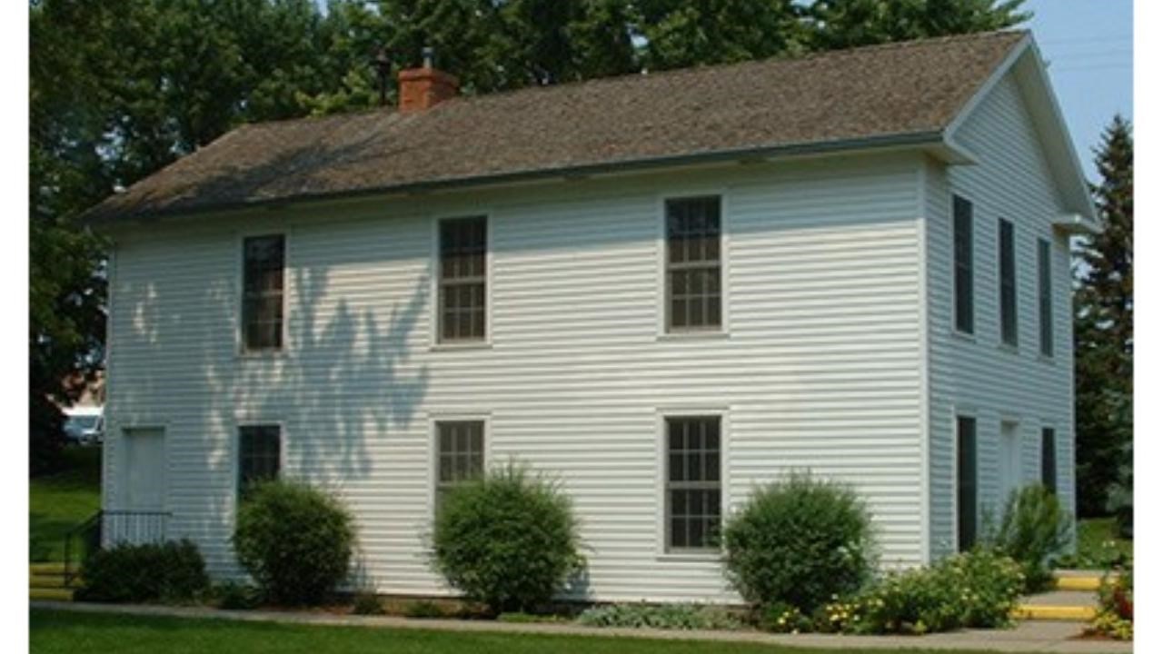 Dakota Territorial Capitol Replica with white colored siding and six windows and three green bushes