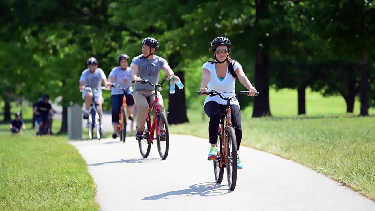 Bicyclists wearing helmets ride on a paved path.