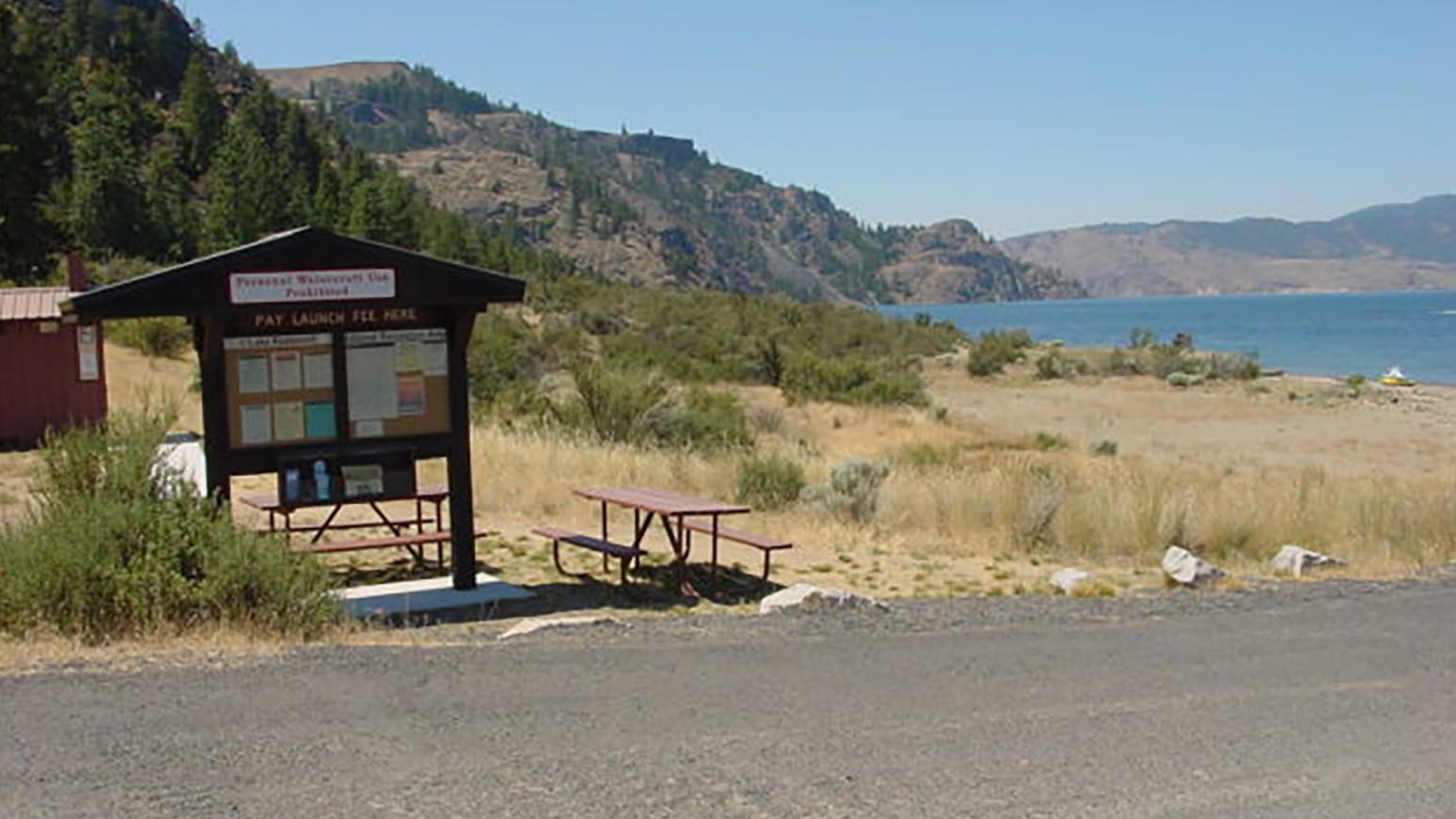 A gravel road, information kiosk, and picnic table on the shores of the lake, next to the launch.