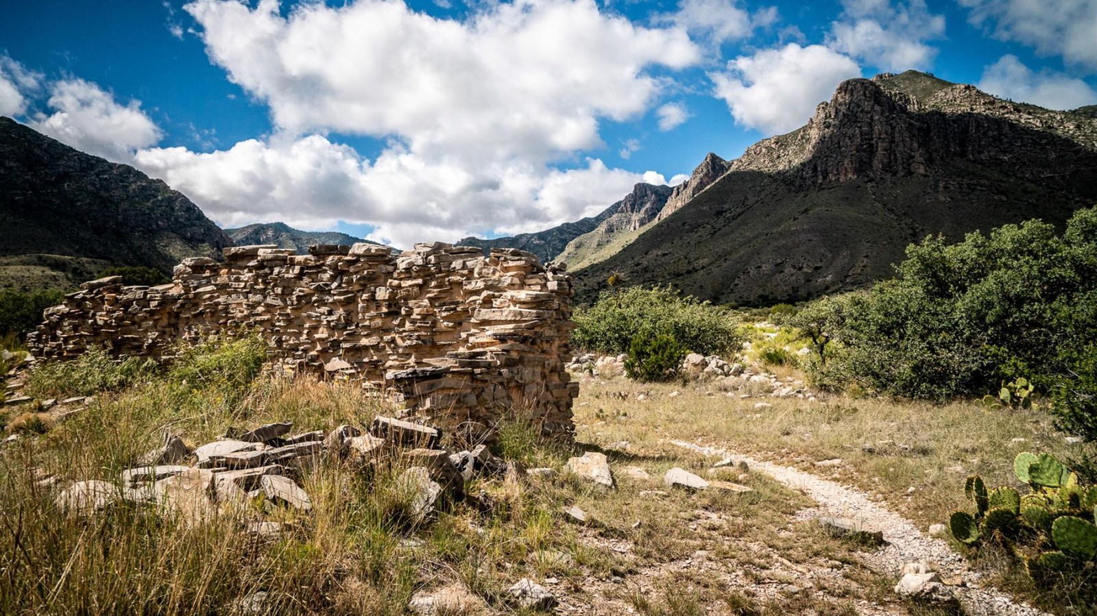 A trail winds past the ruins of a rock wall in a desert landscape