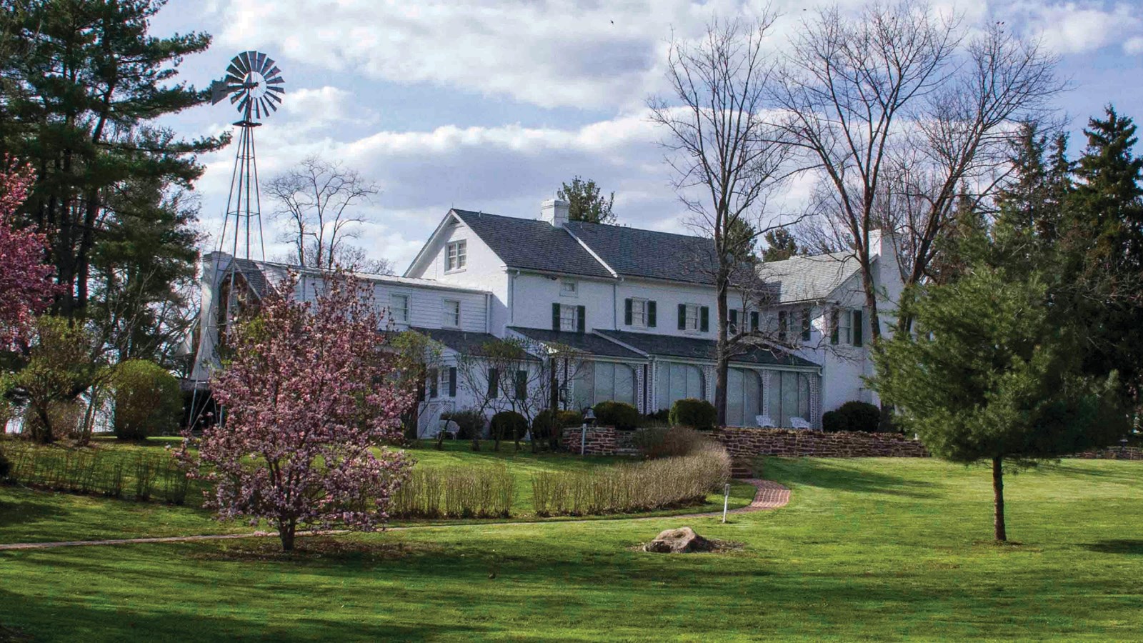 A two story white house surrounded by manicured lawns and gardens.