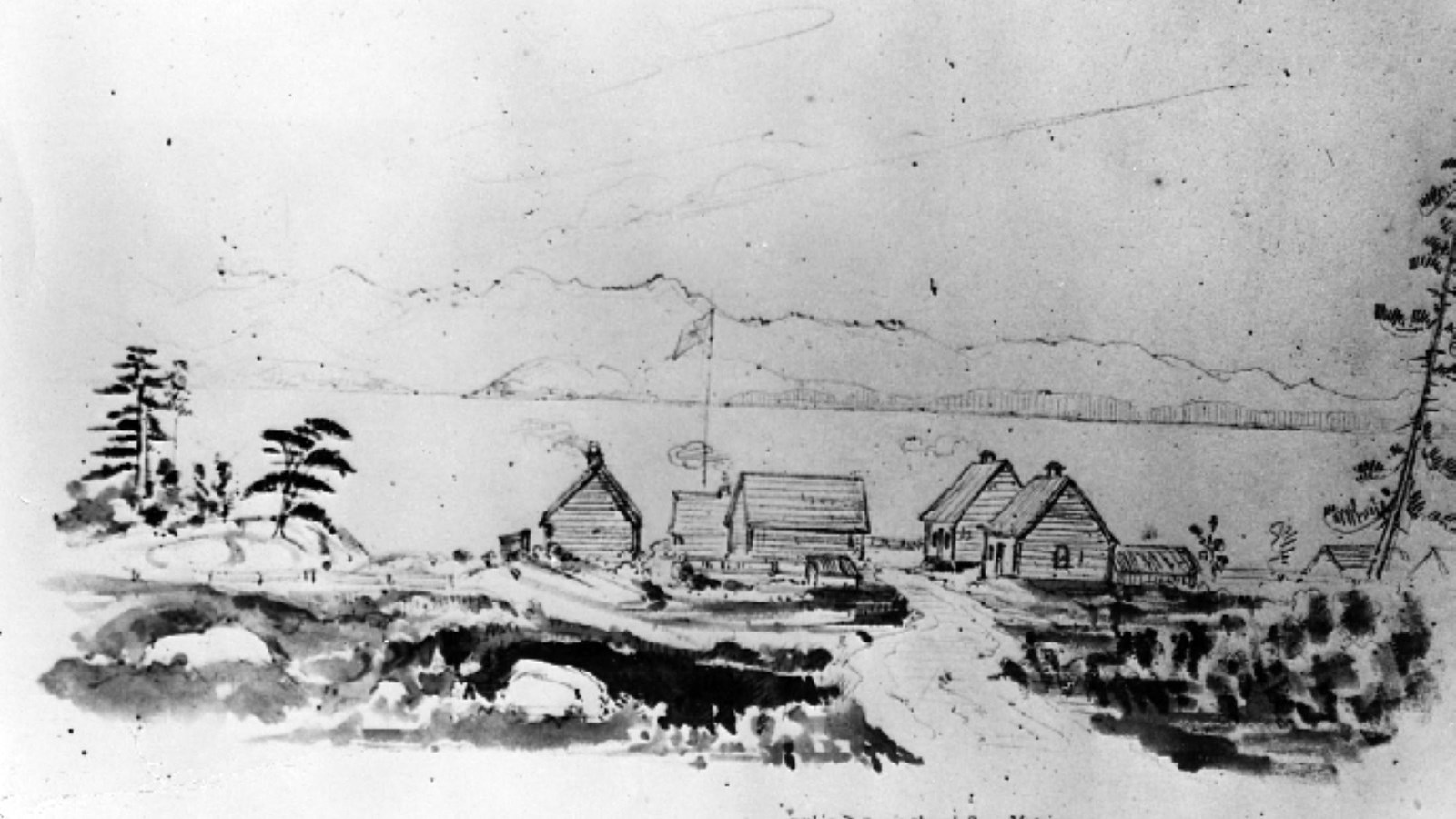 Black and white image of a group of rustic buildings in the forest in front of the ocean