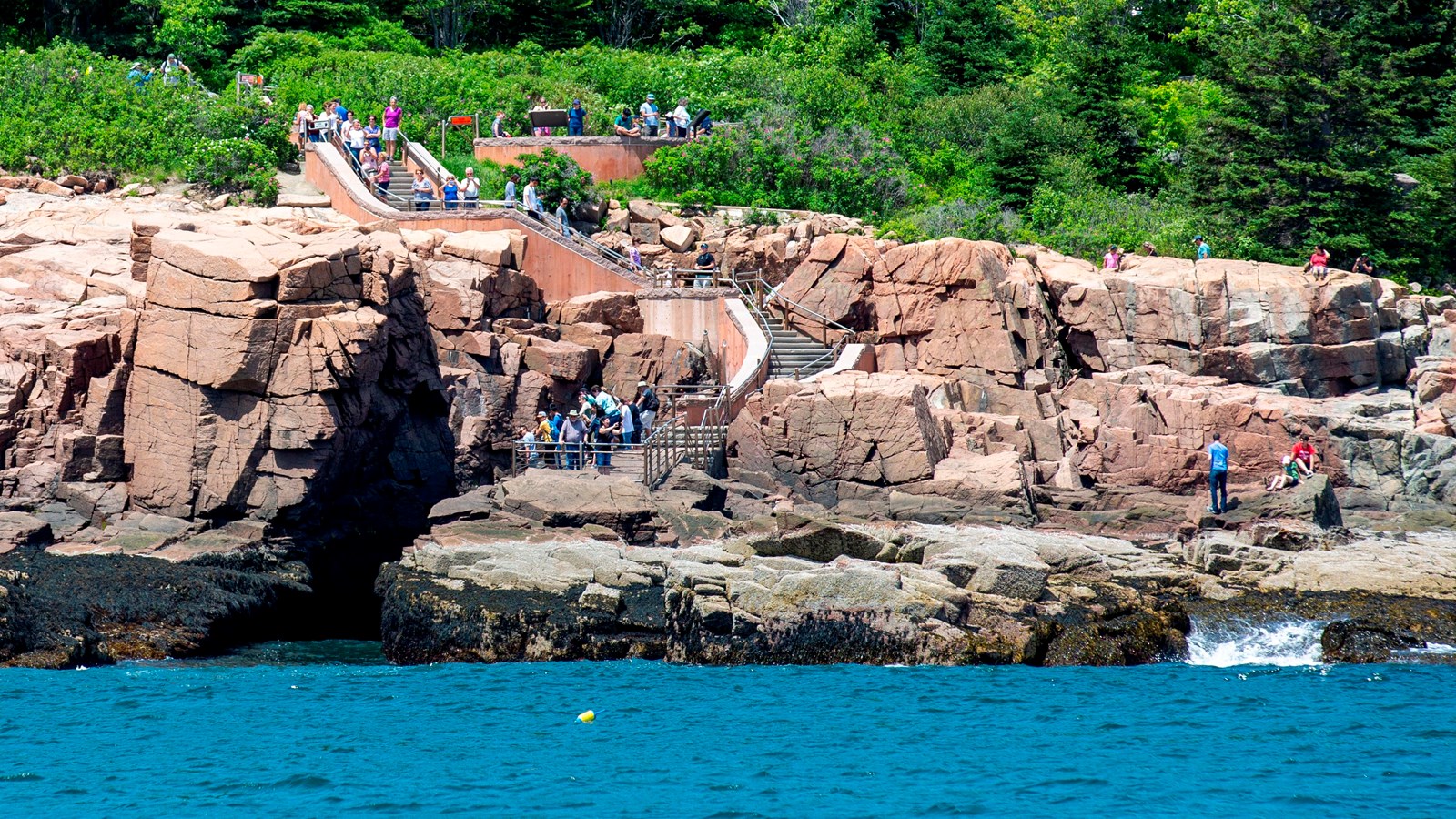 People gather on stairs leading down a cliff from a road to the ocean