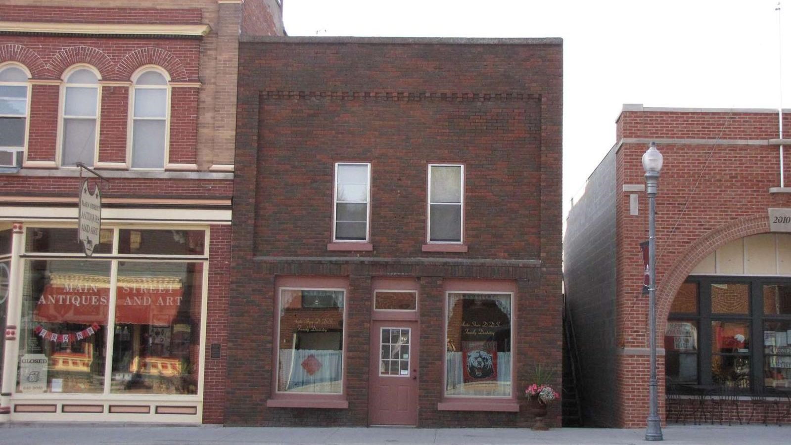 A downtown building is faced with dark red bricks, with two small windows above the storefront. 