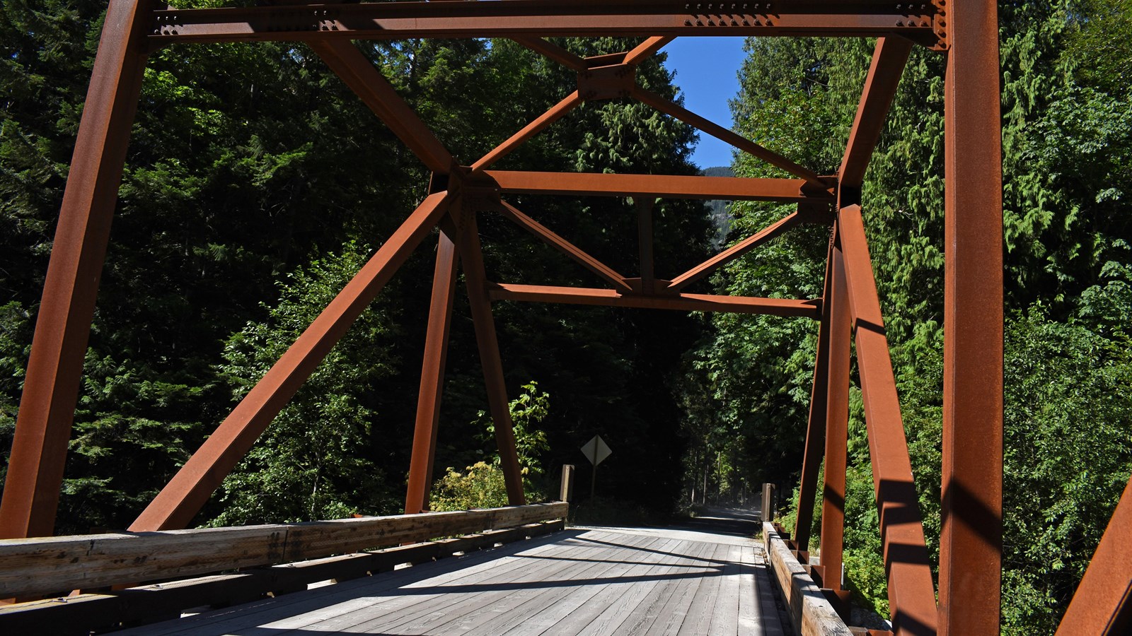 A rusty-brown metal trussed bridge.