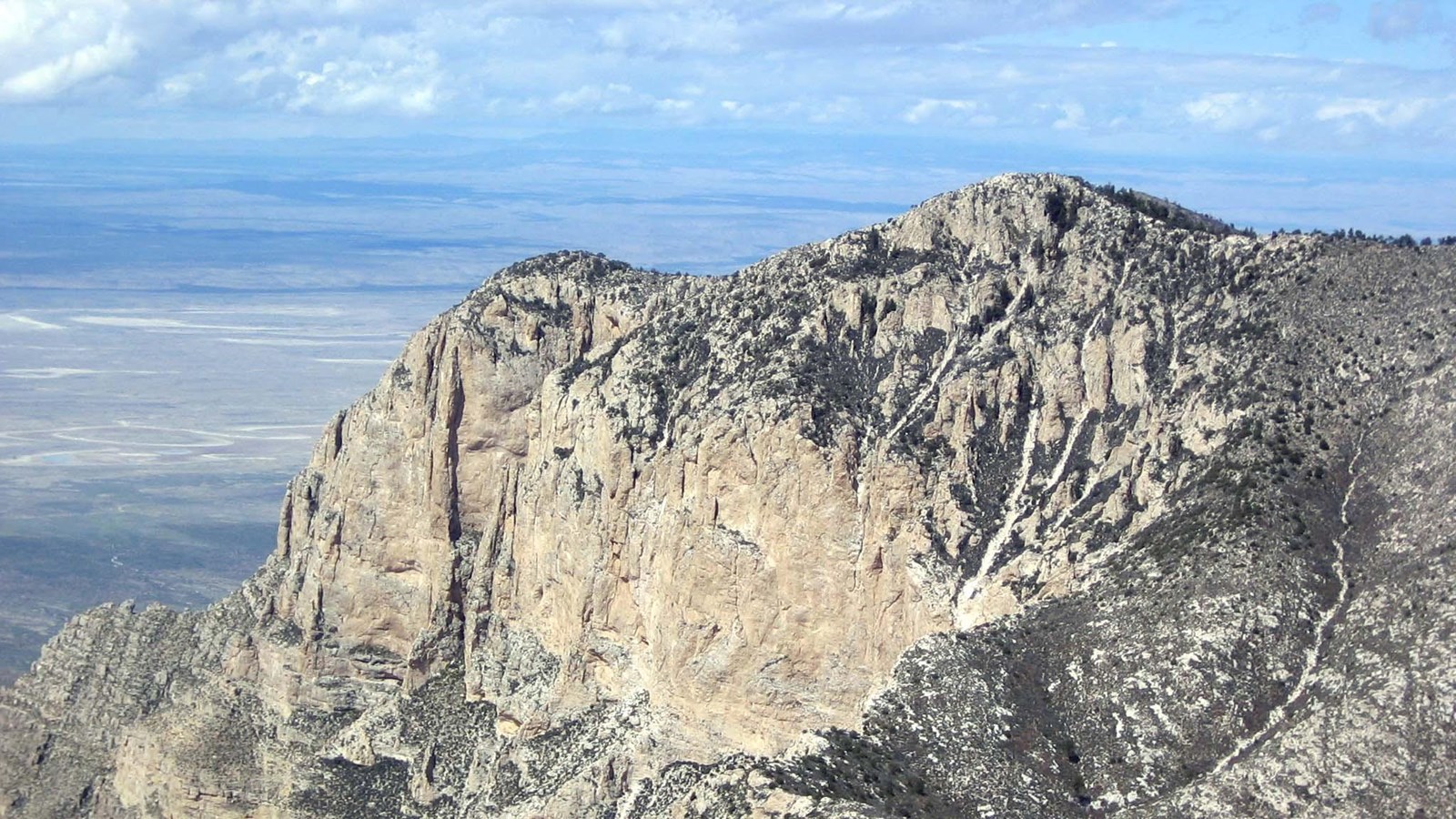 A yellow cliff face rises in the distance, defining a mountain peak. 