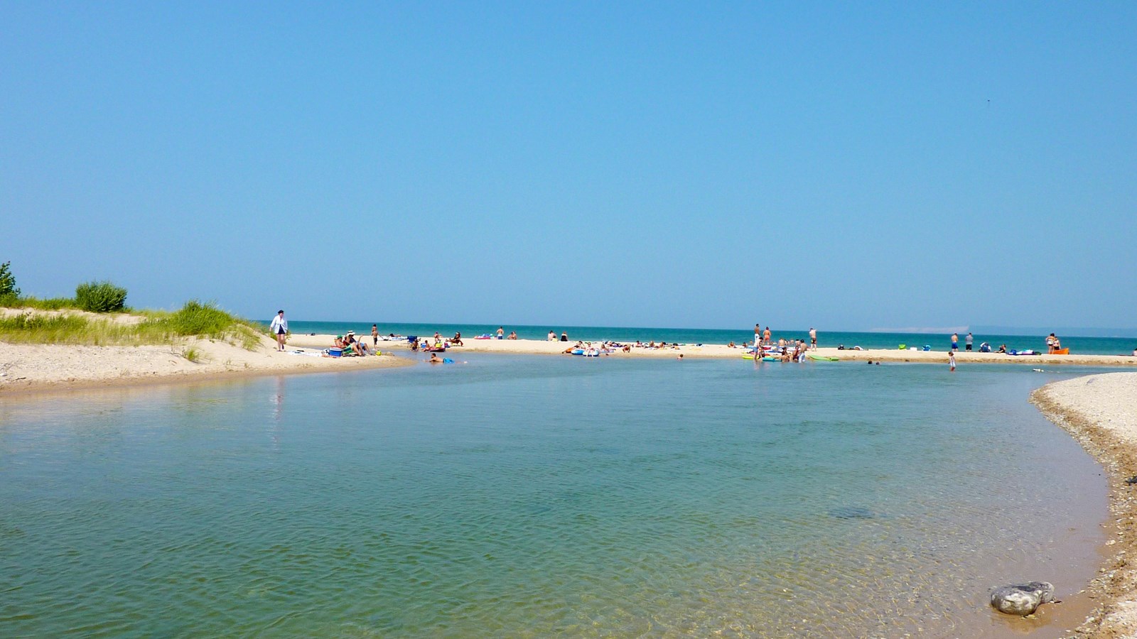 Clear, bright blue water of river winds toward bar of sand and a large lake