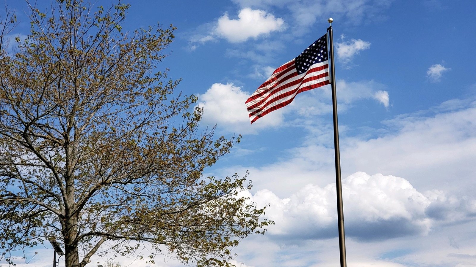 The American flag with red and white stripes and white stars against a blue sky.