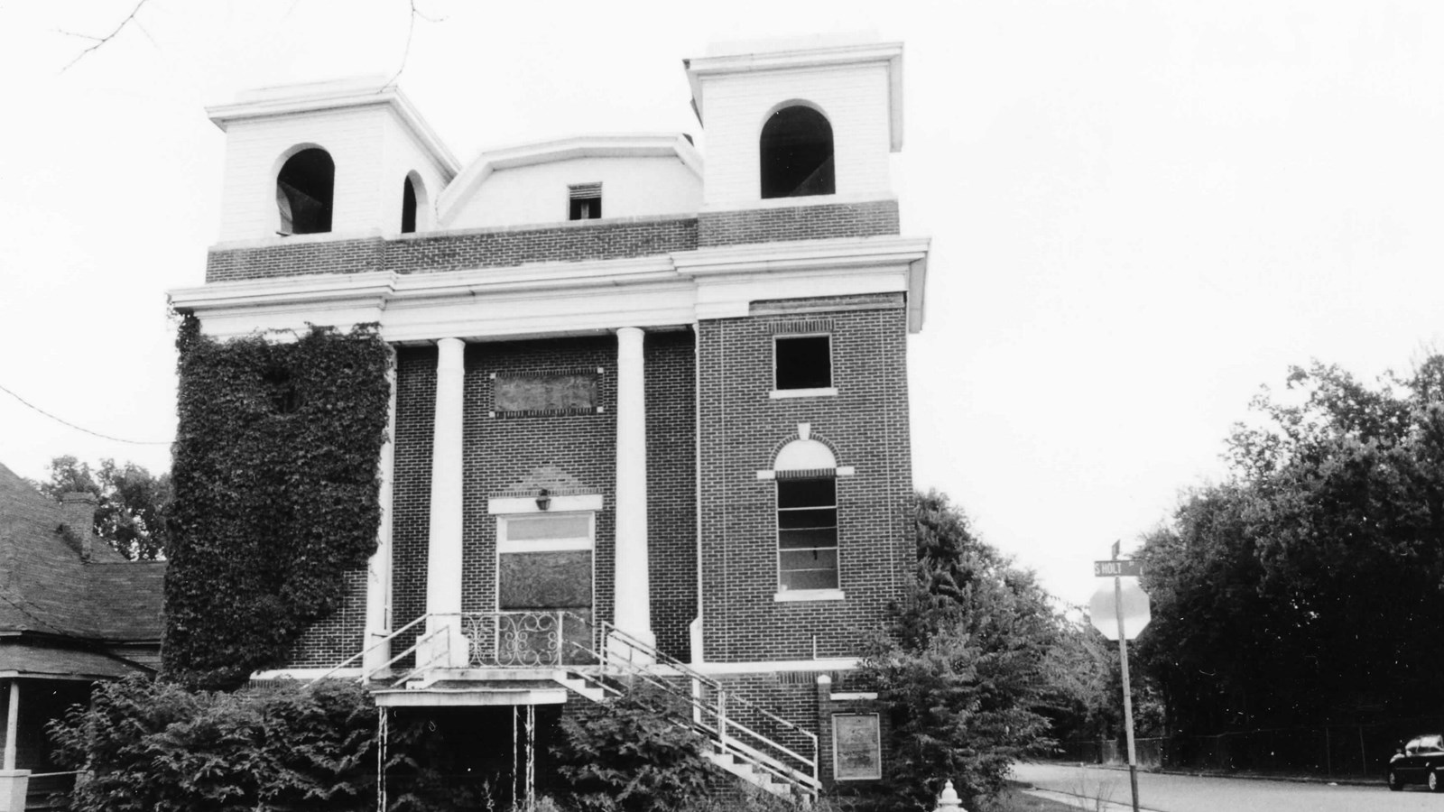 Brick classical revival-style church, with vegetation growing outside