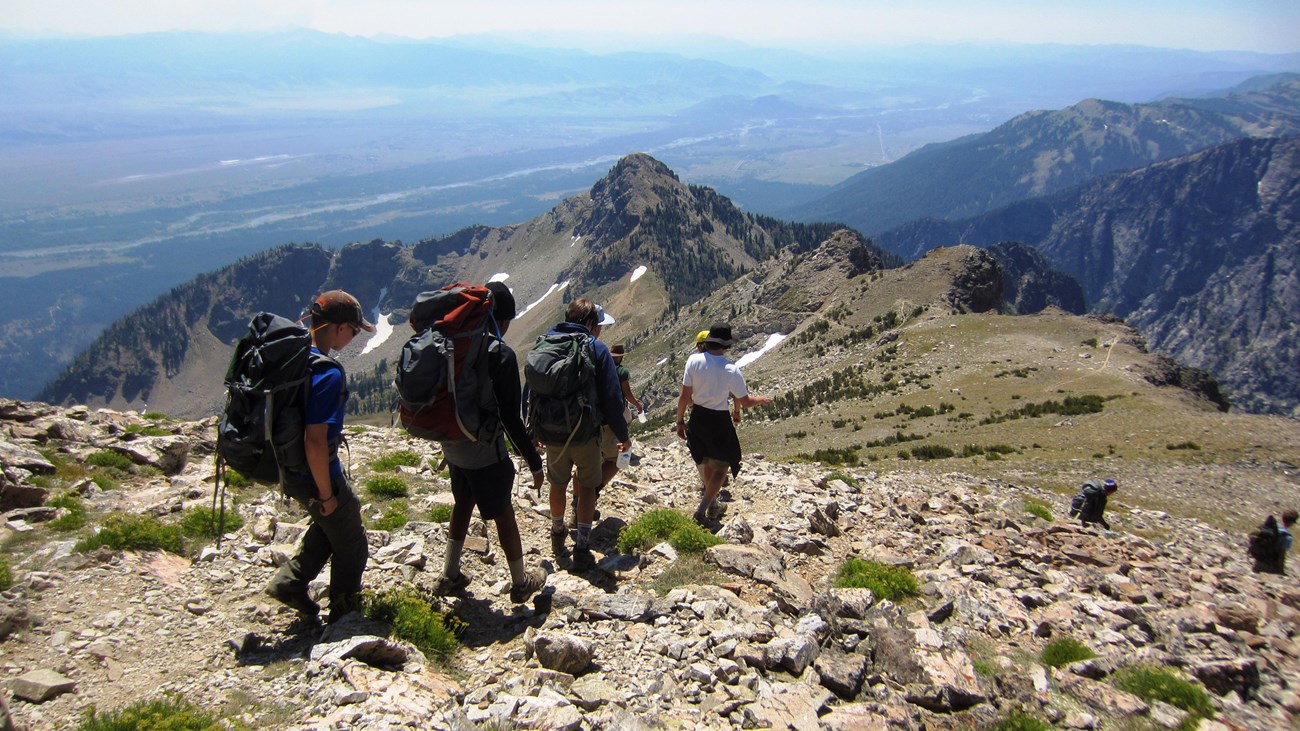 Four hikers walk down a steep, rocky trail.