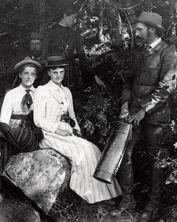 B&W photo of group in 19th century dress posing among rocks and trees