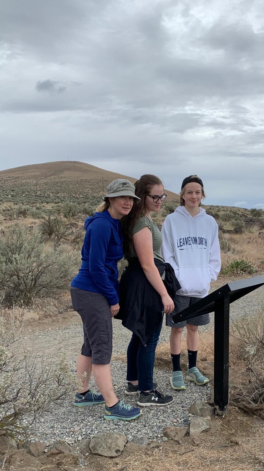 Color photograph of 3 women standing in front of an informational display in the shrub steppe.