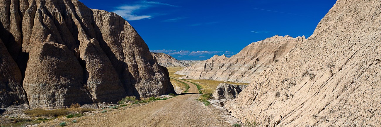 a dirt road leads between the low point of two buttes with a vibrant blue sky ahead.