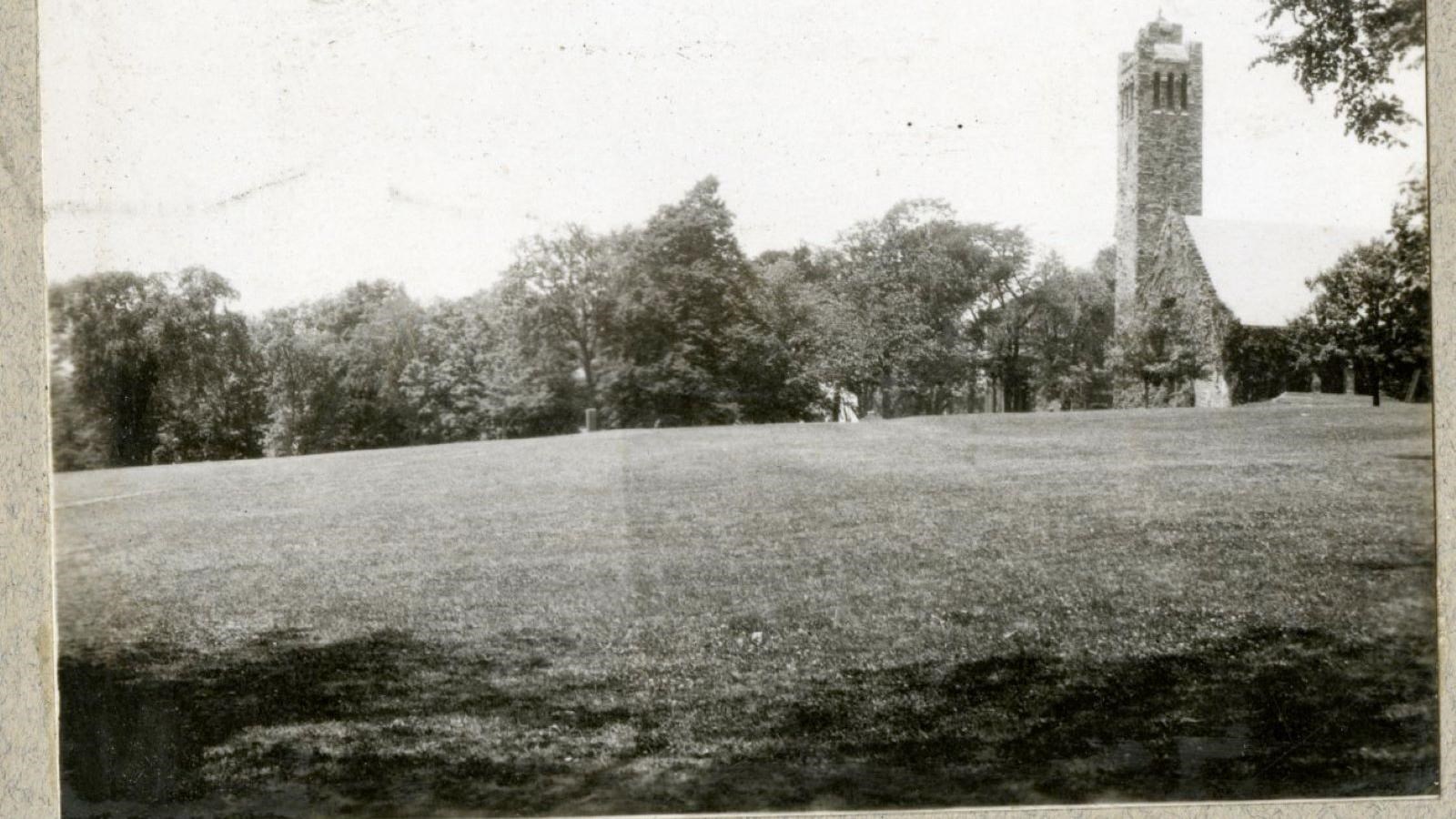 Black and white of grassy open area with trees on the far edge with a large stone tower