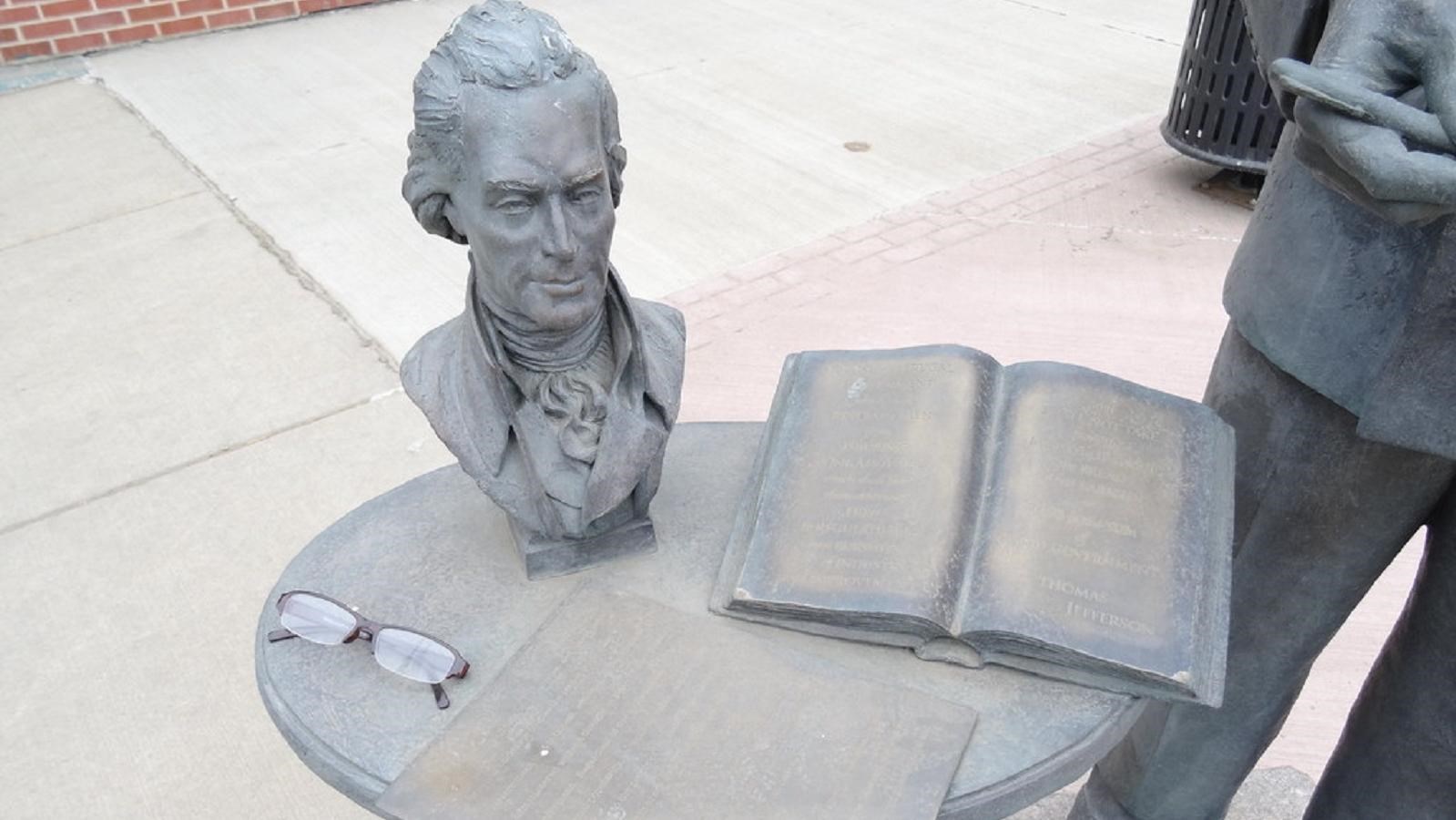 A bronze statue consisting of a bust, book, and pair of glasses on a table.