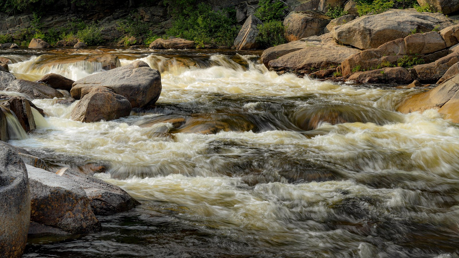 White water rushes between large boulders to form short waterfalls in the stream