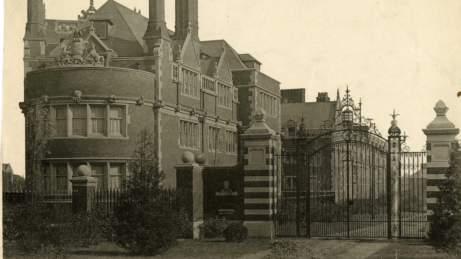 Black and white of large brick building with flat grassy area in front with gate to access building
