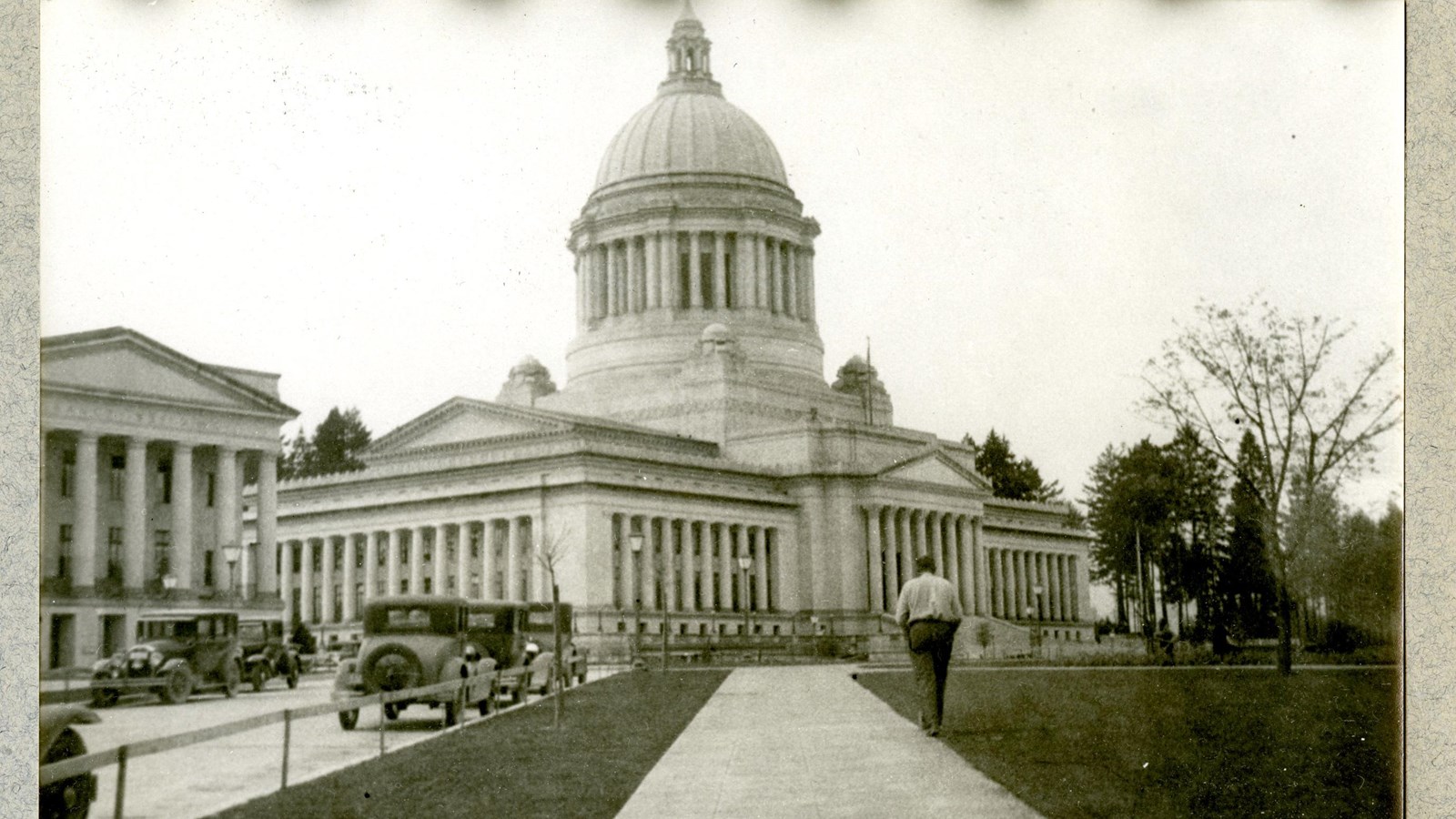 Black and white of road leading to large domed capitol building with person walking along