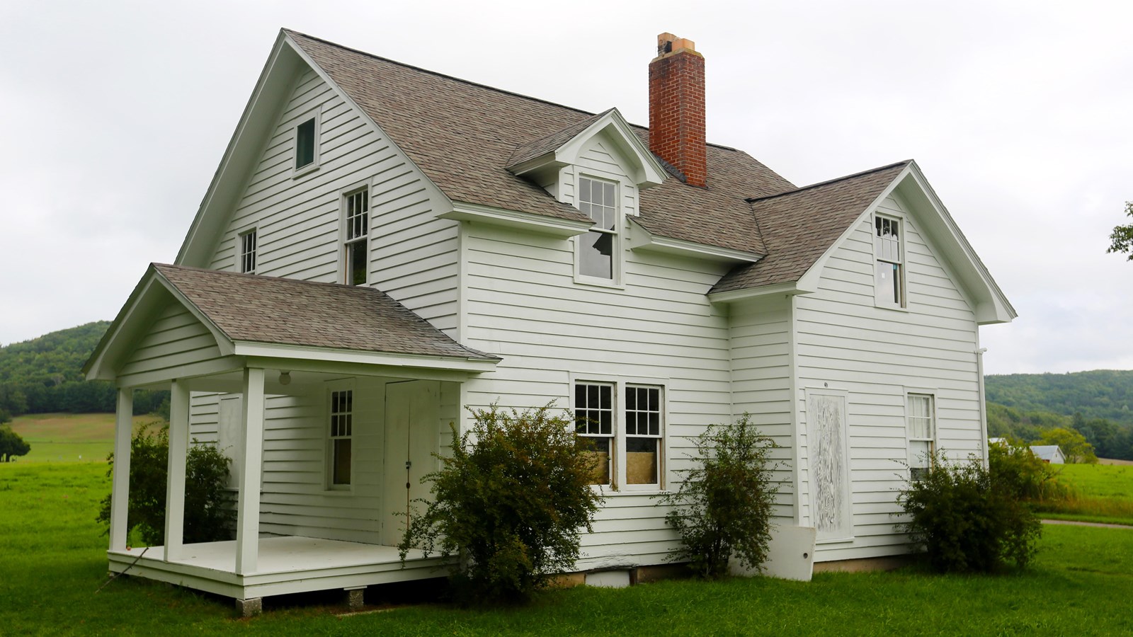 A white, many gabled farmhouse with covered front porch sits on a green lawn