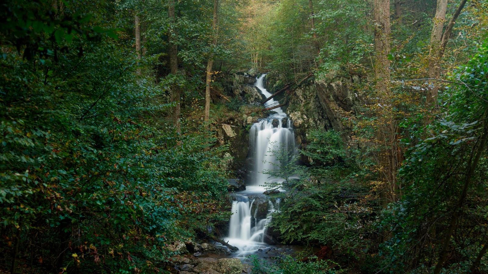 A color photograph of a tall waterfall in the forest. 