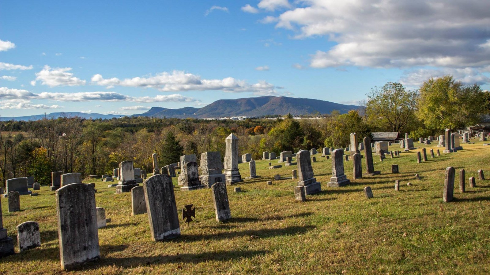 Thin, weathered gravestones mark graves on a hill in a mountain valley.