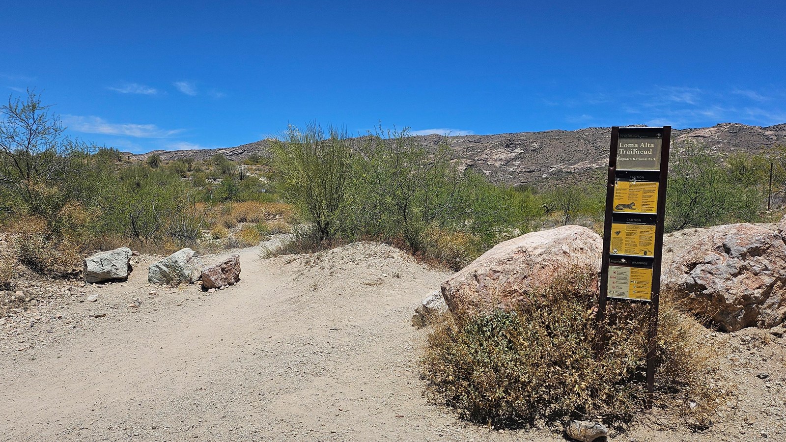 A tall sign stands in the right of the image, a dirt trail spans to the left & into the distance