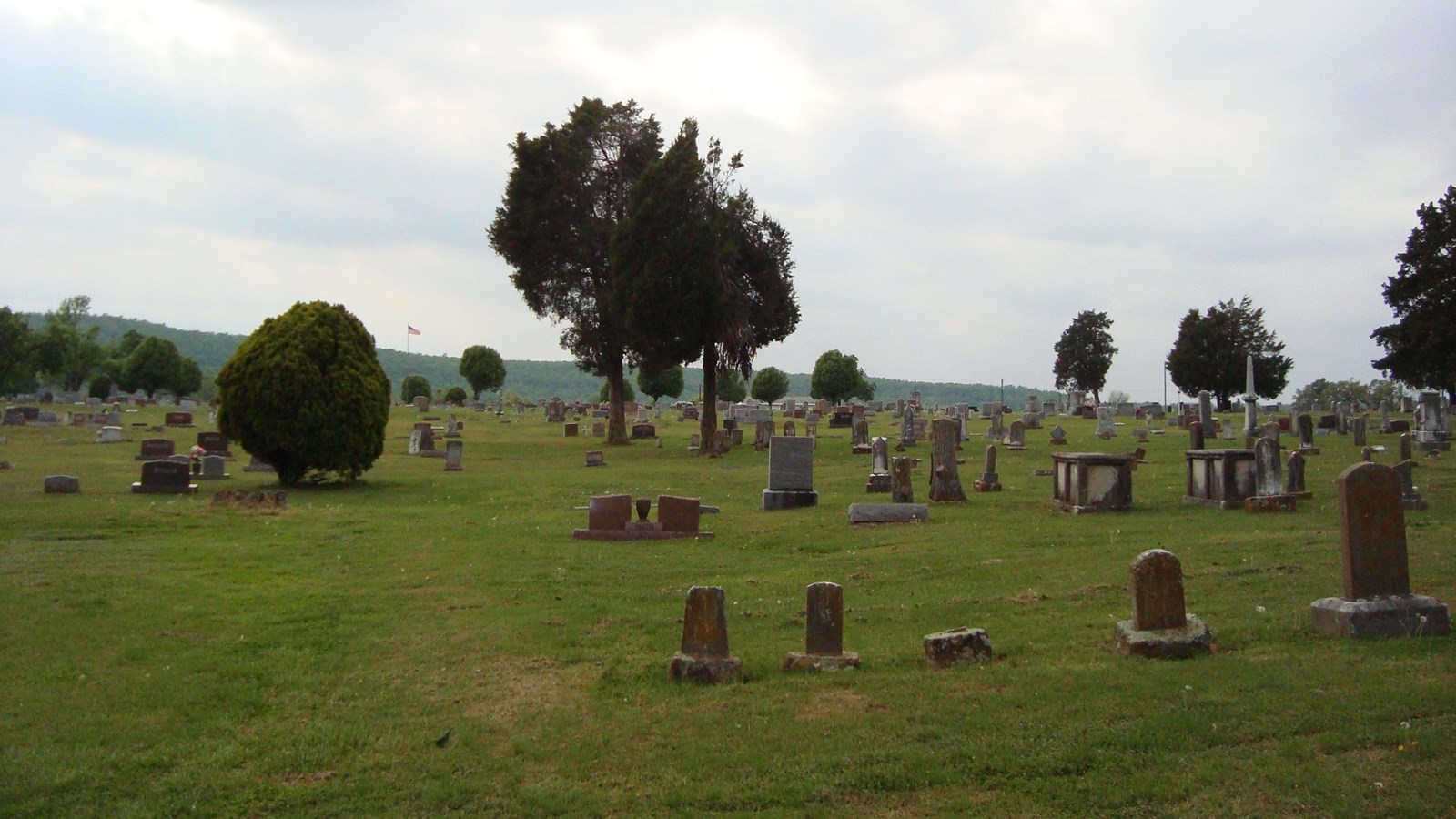 An expansive view of a flat, grassy cemetery dotted with headstones and a few deciduous trees.