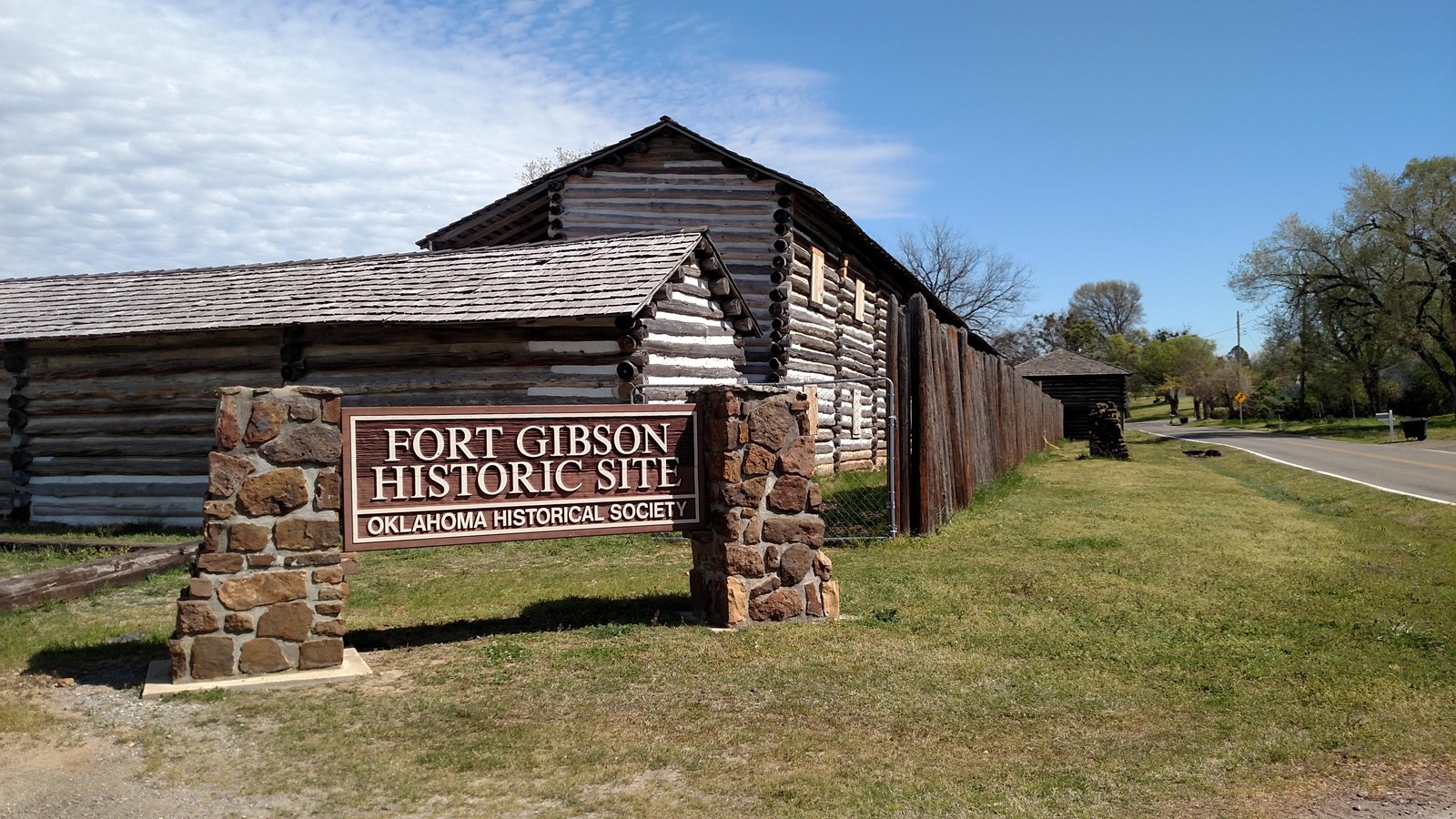 A stone sign sits in front of large historic log fort 