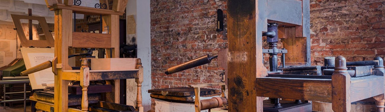 Color image of two wooden 18th-century printing presses with a brick wall in the background.